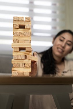 Kırılgan bir istifleme kulesini dikkatlice analiz eden bir kadının hangi tahta bloğun kaldırılacağına karar verirken odak, strateji, denge ve gerilimi vurguluyor..