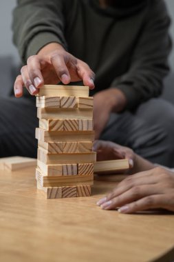 Dengesiz bir istif kulesinin tepesine ahşap bir blok yerleştiren bir adamın yakın plan çekimi odak, kontrol, denge ve kapalı masa üstü oyununda başarıyı yakalıyor..