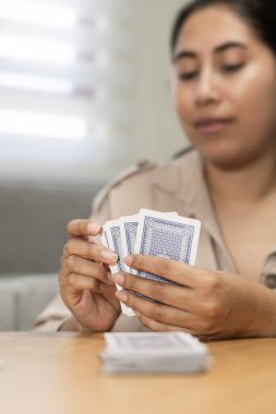 Kart oyunu sırasında oyun kartlarını dikkatlice inceleyen bir kadının yakın plan çekimi. Konsantrasyon, strateji ve karar verme mekanizmasını rahatça iç mekanda vurgulamak..