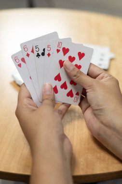 Bir masa başı kart oyunu sırasında el ele tutuşan bir kadının yakın plan görüntüsü, odak, strateji, beklenti ve evde dikkatli oyun oynamanın vurgulanması.