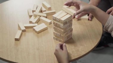 Bir oyun sırasında sabır, odaklanma ve dikkatli dengeyi gösteren, bir masa düştükten sonra ahşap blok kulesini yeniden inşa eden ellerin yakın çekimi.