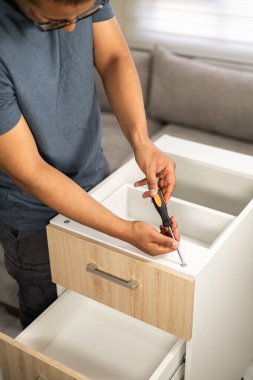 Bir marangoz bir çekmece sapının vidalarını bir tornavida kullanarak ayarlar, kapalı mobilya montajı sırasında detay ve hassasiyete odaklanır.