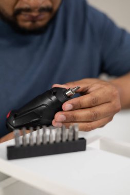 Kapalı mekanda mobilya monte etmeye hazırlanırken tornavida ve değiştirilebilir parçaları tutan birinin elleri..