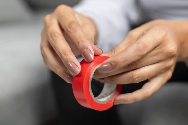 Kapalı bir masada makasın yanında kırmızı bir kurdele tutan eller, basit bir zanaat hazırlamak ya da kesme işi.