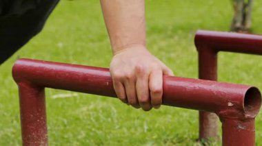 Adam yere paralel çubuklar kullanarak şınav çekiyor. Açık hava antrenmanı sırasında güç, kontrol ve yoğun vücut ağırlığı eğitimi gösteriyor..