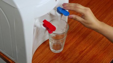 Bir insanın bardağını bir ev içindeki su dağıtıcısının içme suyuyla doldurup temiz su tüketimini ve günlük rutin rutinini gösteren yakın plan..