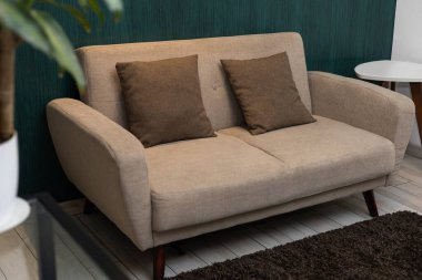 Modern bir evde sergilenen bej renkli döşeme koltuğu yumuşak dokuları, nötr renkleri ve basit mobilya tasarımını ön plana çıkarıyor..