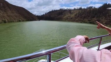 Birkaç turist, sakin bir göle ve manzaralı bir tekne gezisi sırasında etrafındaki dağlara hayran oldukları için ellerinde bir tekne rayı tutuyorlar..