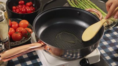 Bir kadın sıcak tavaya yağ döker, ev yapımı bir yemek hazırlar, mutfak aktivitelerini ve pişirme sürecini ön plana çıkarır..