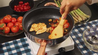 Tavukla domatesleri karıştırmak için ahşap bir kaşık kullanarak ellerinizi kapatın, pişirme işlemini, yemek hazırlama ve mutfakta ev yapımı yemeği gösterin..