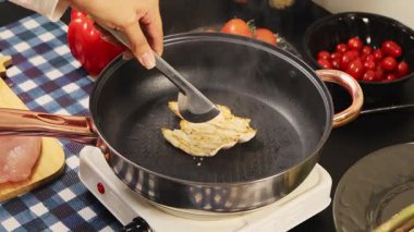 Sıcak tavada maşa kullanarak tavuğu çeviren ellerinizi kapatın. Yemek pişirme, yemek hazırlama ve mutfak düzeninde ev yapımı yemekleri gösterin..