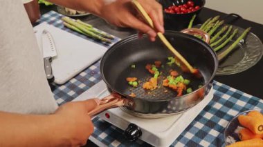 Ahşap kaşık kullanarak sebzeleri karıştıran, pişirme, yemek hazırlama ve mutfakta ev yapımı sağlıklı yemekleri gösteren ellerinizi kapatın..