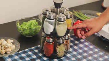 Baharat rafını çevirerek taze malzemelerle çevrili özel bir çeşni seçmek, pişirme hazırlığını ve mutfak düzenini temsil eden bir eli kapatın..