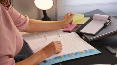 Masasından ajandasından yapışkan bir not alan bir kadının yakın çekimi. Görüntü, modern bir ofis veya işyerinde organizasyon, planlama, üretkenlik ve detaylara dikkat eder..