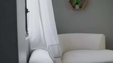 Hafif bir esinti oturma odasının perdelerini hareket ettirir, huzurlu ve havadar bir atmosfer yaratır. Nazik hareket, doğal ışığı, sakinliği ve iç mekanın sessiz güzelliğini vurgular..