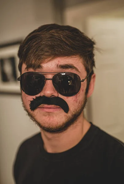 man wearing a fake moustache and sunglasses is trying to disguise himself