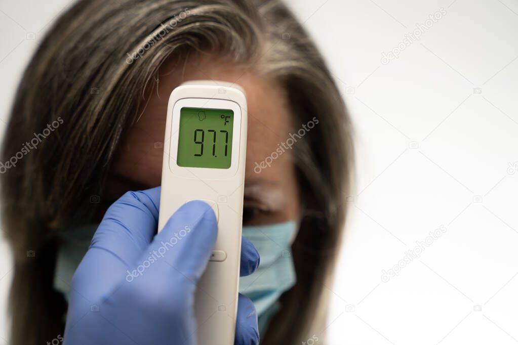 gloved hand holding a thermometer that displays 97.7 without a fever