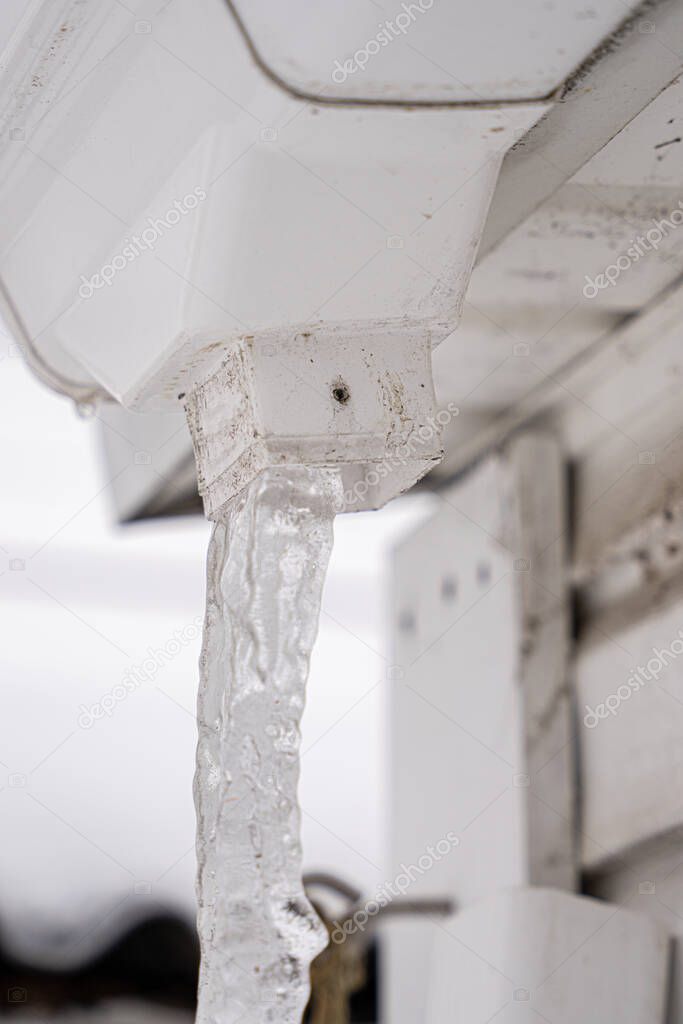 icicle hangs from a gutter that has been frozen and blocked by an ice dam
