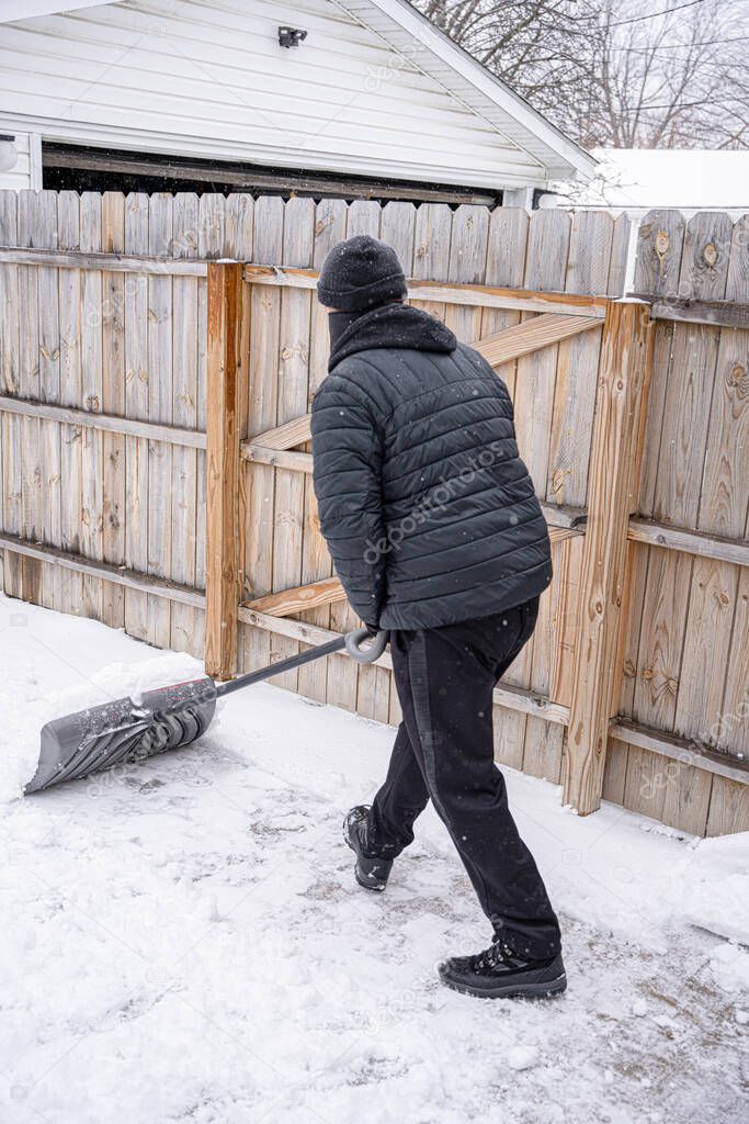 man is using a snow shovel to clear your sidewalk and driveway after a recent snow storm