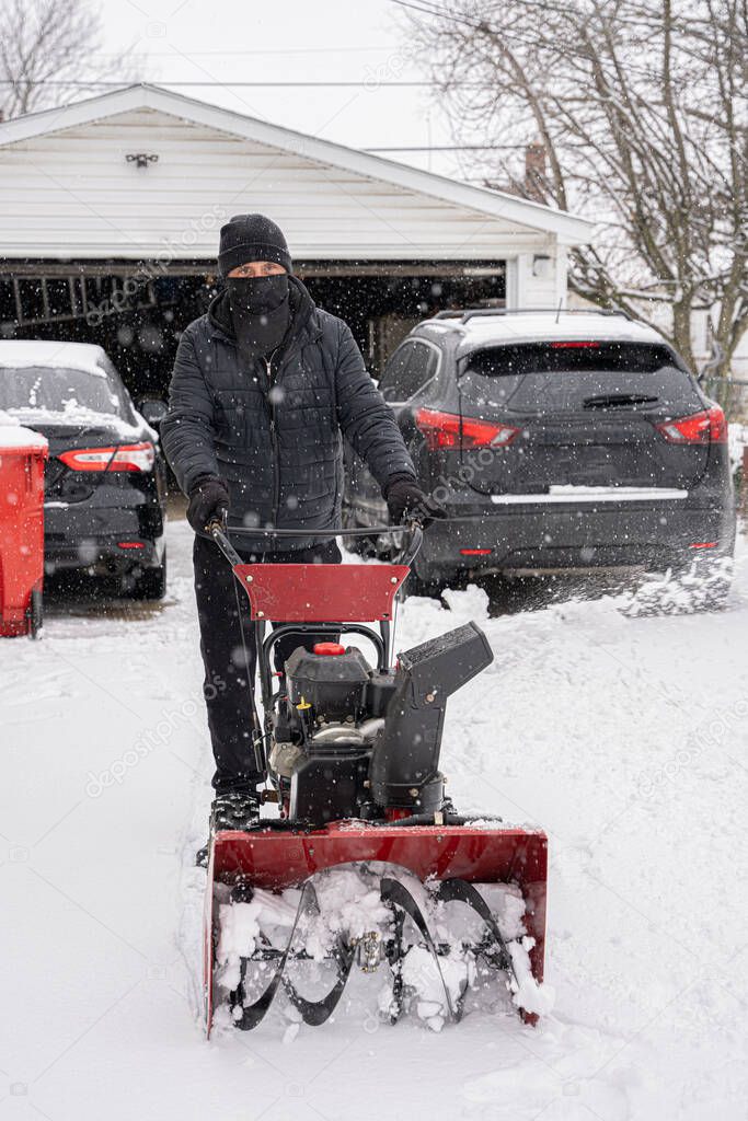 man snowblows a driveway to clear the path after a heavy snow storm
