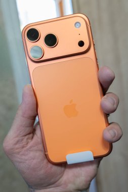 İnsan eli yeni bir iPhone 17 Promax tutuyor. Yeni renkli kozmik turuncu rengin yanı sıra yeni kamera, flaş ve Lidar sistemi son modelden sonraki yıl için yeniden dizayn ediliyor.