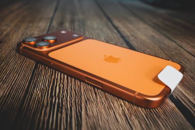 Iphone 17 Pro Max kozmik turuncu bir tabloda, parlak tasarımı ve üçlü lens kamera sistemi ile sığ bir alan derinliği ve mobil teknoloji ve endüstriyel estetik modern eğilimleri temsil eden bir ahşap masada yatıyor..