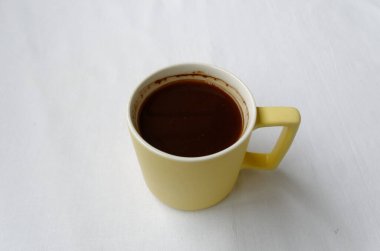 Nazikçe sarı, saplı beyaz kupa, yukarıdan beyaz arka plan manzaralı, canlandırıcı kokulu sabah kahvesi.