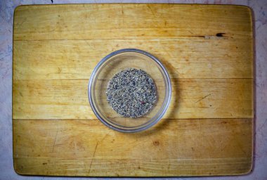 Ahşap bir tahtanın üzerinde cam bir kasede duran karabiber.