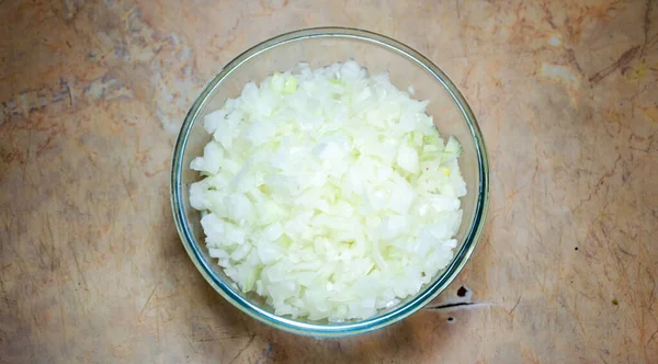 Finely cut onions in a glass bowl on a light table — Stock Photo, Image