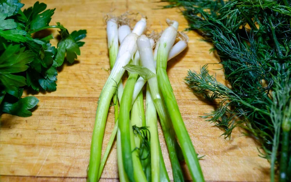 Hojas de cebolla verde, perejil y eneldo en una tabla de cortar de madera —  Fotos de Stock