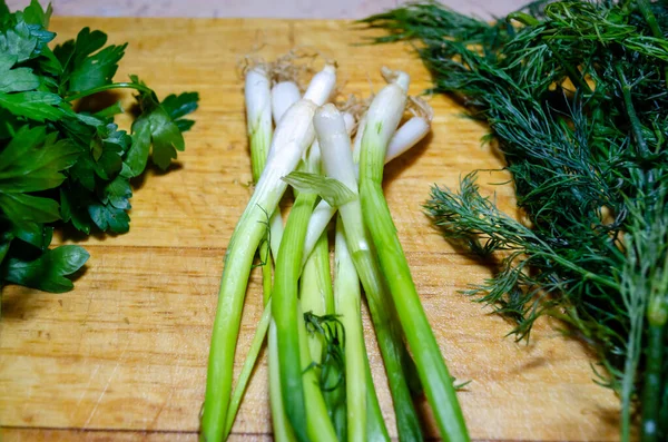 Hojas de cebolla verde, perejil y eneldo en una tabla de cortar de madera —  Fotos de Stock