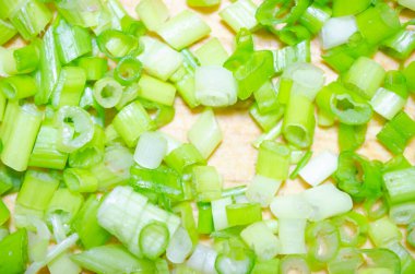 Sebzeleri yakın planda kesmek için ahşap bir tahtanın üzerinde yeşil soğanları ince ince doğradım.