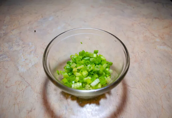 Cebolas verdes finamente cortadas em um boliche de vidro em uma mesa leve — Fotografia de Stock