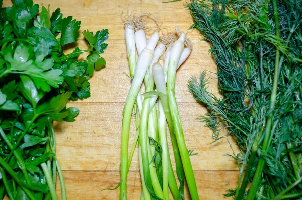 Hojas de cebolla verde, perejil y eneldo en una tabla de cortar de madera —  Fotos de Stock