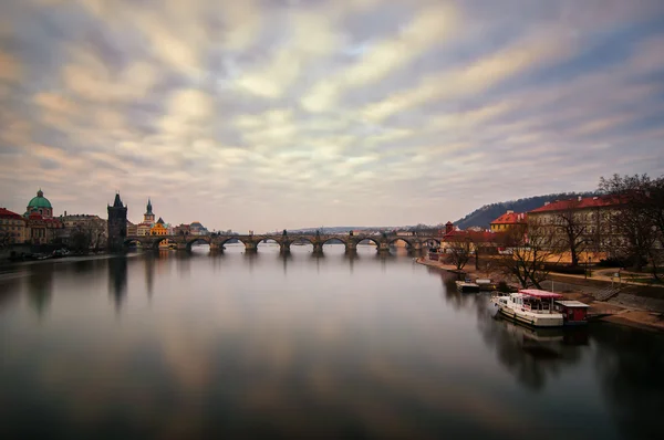 Belo nascer do sol perto da famosa Ponte Charles com céu nublado e reflexo de água. Ponte com torre incrível e estátuas antigas no início da manhã. Dia ensolarado típico em Praga, República Checa . — Fotografia de Stock