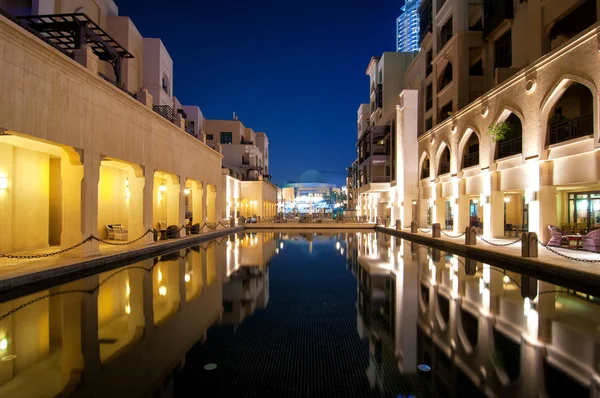 Colorful reflection of souk building in Downtown area during calm night. Calm water in hotel and restaurant pool. Dubai, United Arab Emirates.