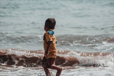 Sahilde dalgalarla oynayan bir çocuk. Un nio jugando on la playa con las olas.