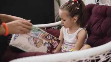 Küçük tatlı bir kız salıncakta oturup annesiyle kitap okuyor.. 