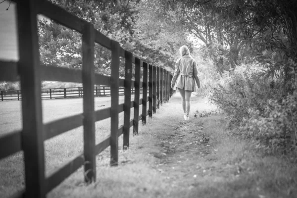 Thoughtful Woman Walking Away Along Fence Outdoors, Black And White. High quality photo