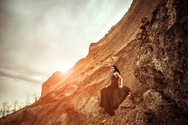 Pretty woman on the sand canyon in long black dress