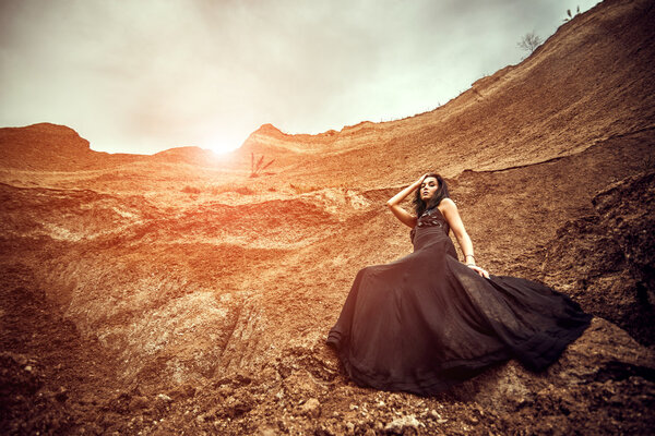 Pretty woman on the sand canyon in long black dress