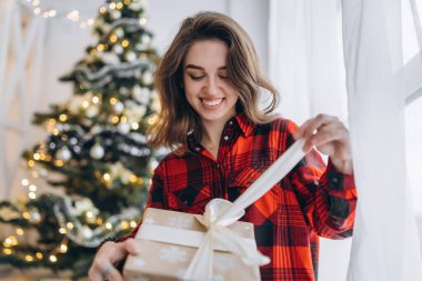 Noel, yeni yıl. Gömlekli ve çoraplı güzel bir kadın Noel hediyesi kutusuyla pencere eşiğinde oturuyor, yeni yıl ağacı arkasında.