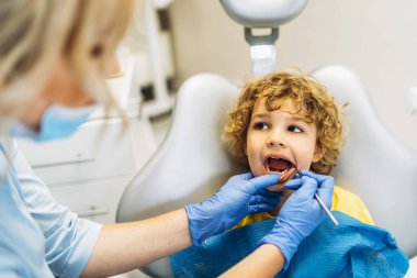 Diş hekiminde dişçiye gidip dişlerini kontrol ettiren sevimli genç bir çocuk.