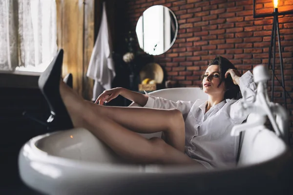 Portrait Beautiful Brunette Lying Empty Bathroom Holding Legs Wearing White — Stock Photo, Image
