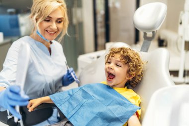 Diş hekiminde dişçiye gidip dişlerini kontrol ettiren sevimli genç bir çocuk.