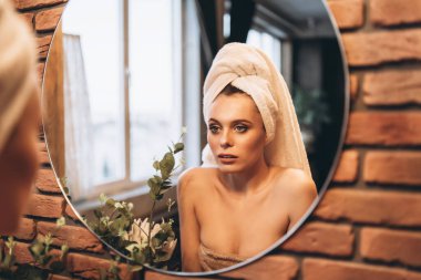 Üzerinde havlu olan güzel esmer kadın banyodan çıktıktan sonra aynanın yanında duruyordu.