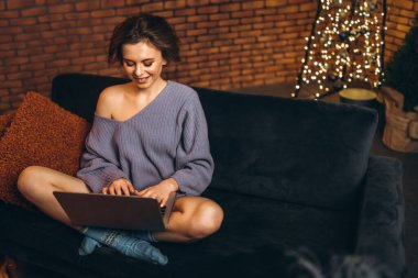 Evdeki kanepede dizüstü bilgisayarı, online eğitimi, eğitimi, alışverişi, çalışma konseptini kullanarak genç bir esmer.