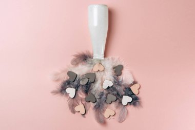 Ahşap kalplerin ve tüylerin yumuşak renkli arka planda şişeden düşüşünün yaratıcı düzlüğü. 