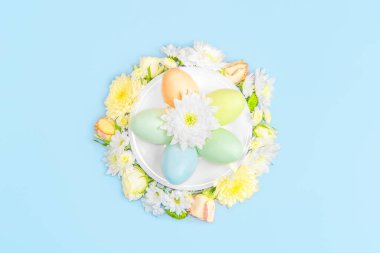 Pastel arka planda çiçeklerin ve paskalya yumurtalarının yaratıcı yerleşimi