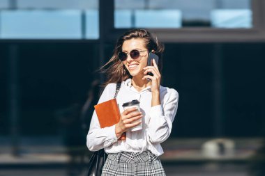 İş kadını cep telefonuyla yürüyor ve konuşuyor. Modern iş merkezinin yakınında. Not defteriyle.